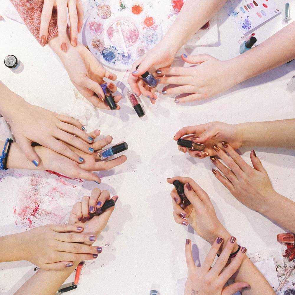 Girls holding bottles of DIY nail polish colors, hands over a table with DIY kit