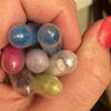 Close up of hand with coral nails holding yellow, blue, red, purple, white, green micas in tubes